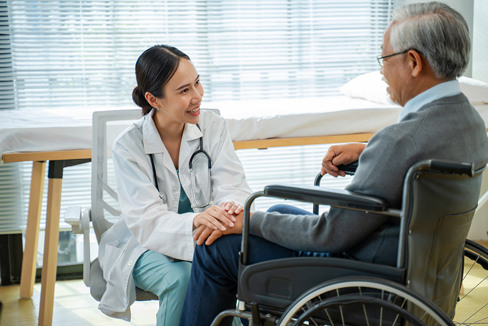 Doctor comforts smiling elderly man in wheelchair during a clinic visit.